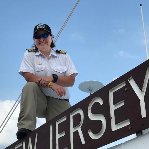 Captain Melissa Velli standing on top of the New Jersey vessel in uniform along with a black Cape May - Lewes Ferry cap
