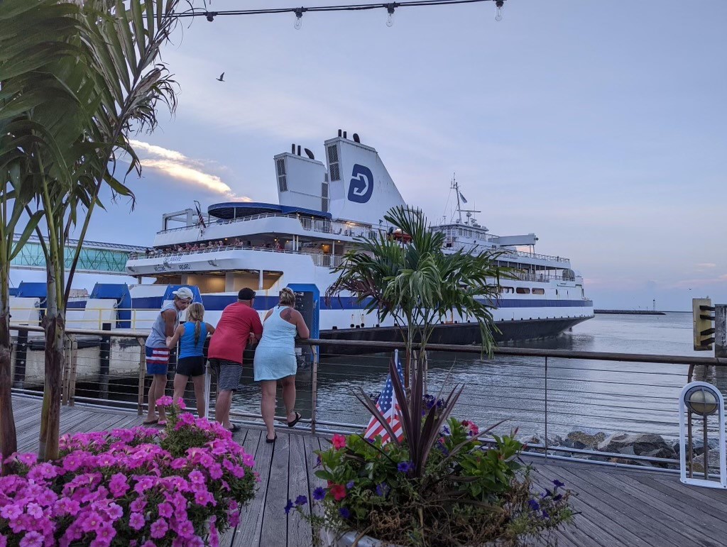 A family leans on the boardwalk railing, looking at the ferry