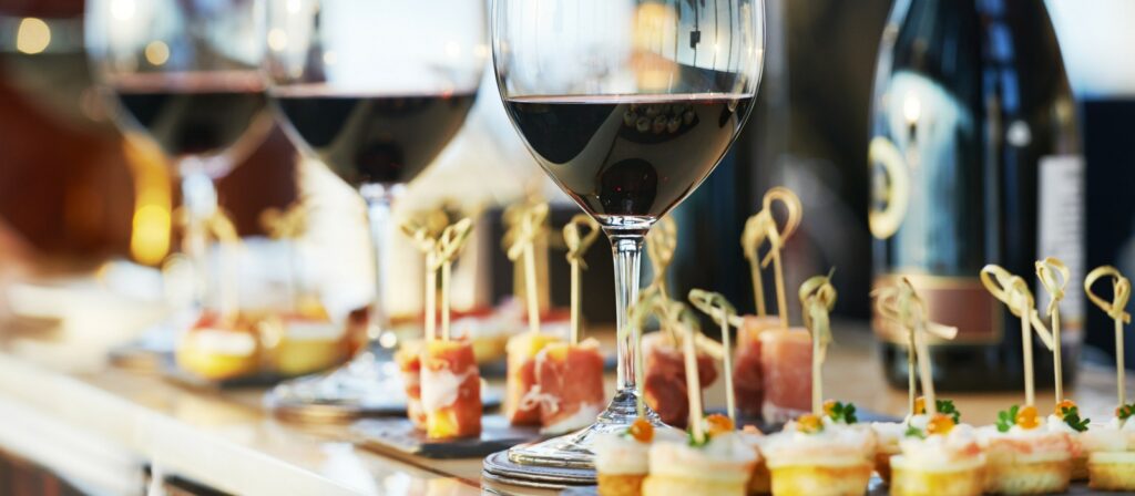 Close-up of red wine glasses and an assortment of catering appetizers, including prosciutto and canapés, promoting the Cape May-Lewes Ferry's banquet and special event services.
