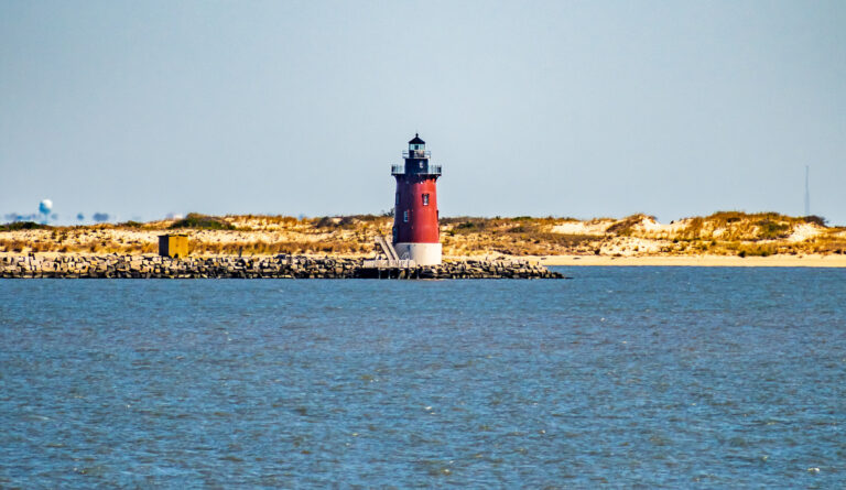 A lighthouse stands in the Harbor of Refuge in Lewes Delaware with beach dunes in the background