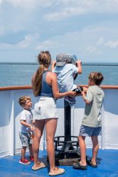 A family enjoys the viewfinder to see the lighthouse and the Harbor of Refuge from the deck of the Cape May - LEwes Ferry as it departs Lewes bound for Cape May.