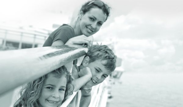 A family of 3 smiles for a photo, leaning on the Ferry deck
